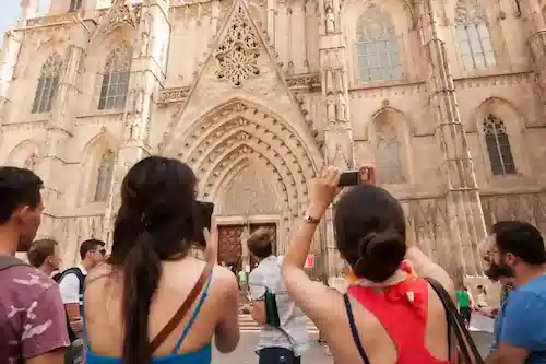 Tourists viewed from behind taking pictures of an ornate Gothic cathedral facade with their smartphones