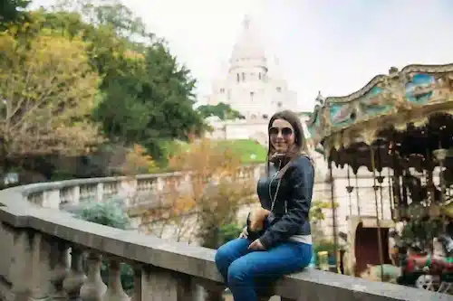 Tourist in a black leather jacket posing near a carousel with the Sacré-Cœur behind her