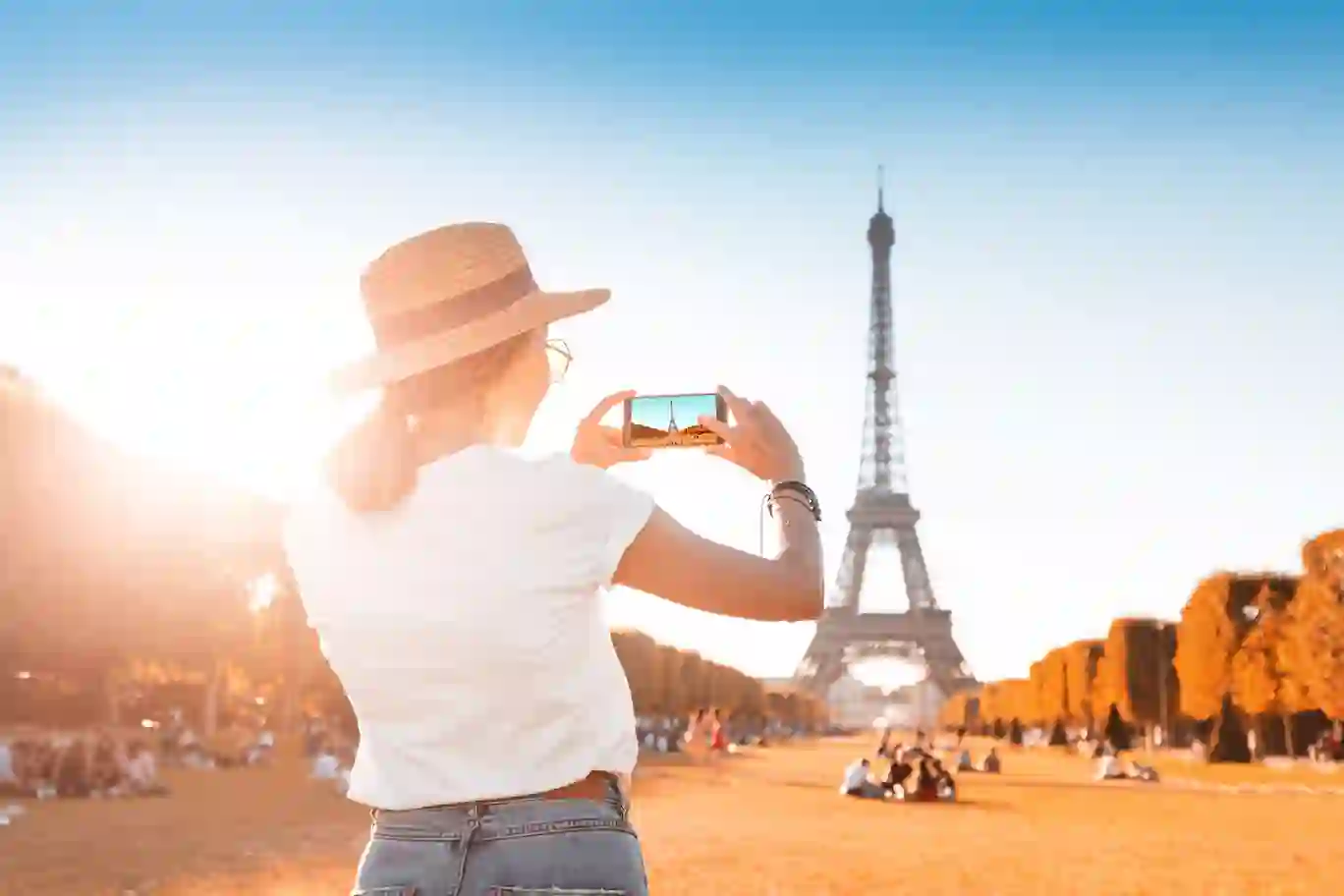 Traveler capturing the Eiffel Tower in Paris with a smartphone on a sunny day.