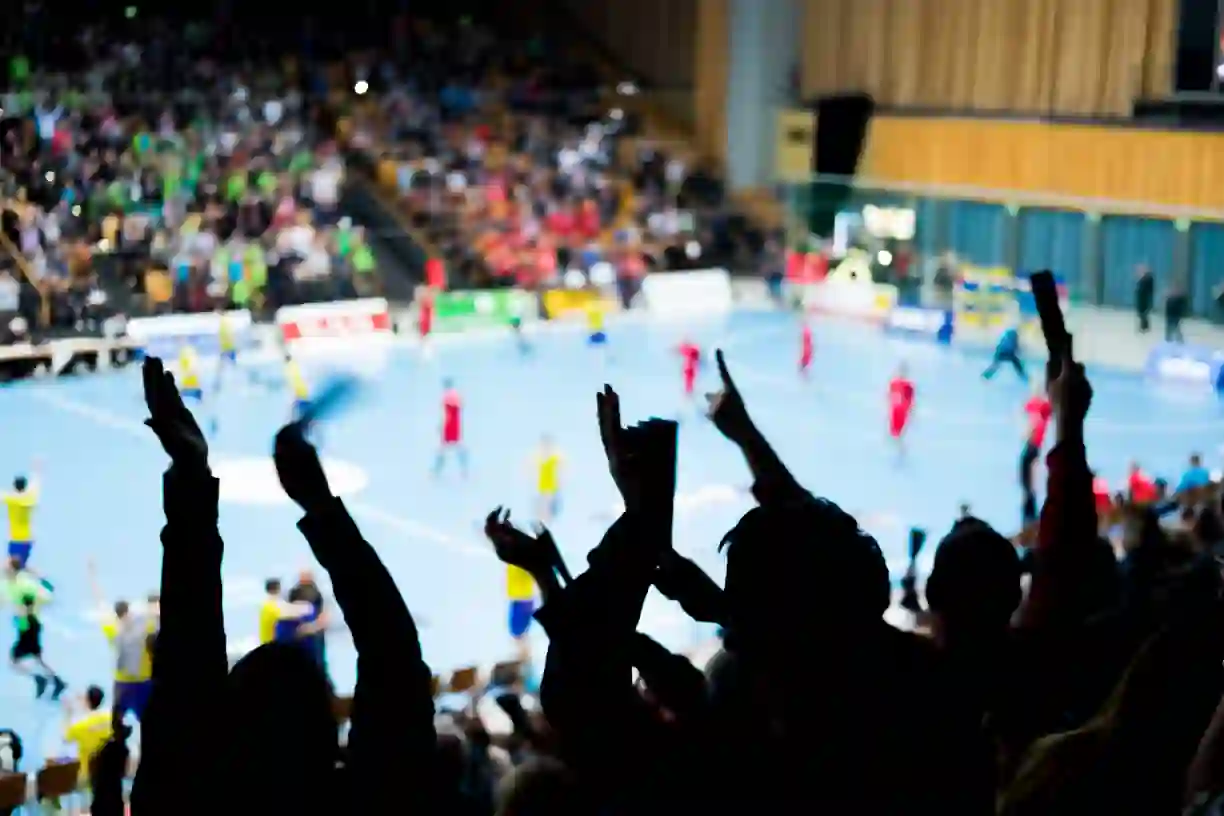 Crowd of spectators with arms raised cheering at indoor sporting event