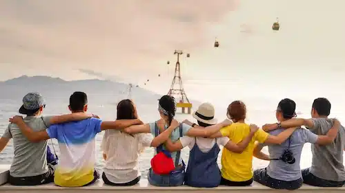A group of friends sitting with their arms around each other looking at a cable car over the water